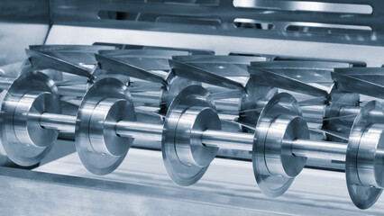 Poster - A machine with a row of metal gears. The gears are silver and are lined up. The machine is in a factory