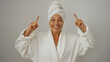 © Krakenimages.com - Mature woman smiling in white bathrobe and towel on head pointing fingers upward against white background