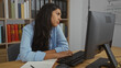 © Krakenimages.com - Young woman working in an office room, seated at a desk with a computer and books in the background.