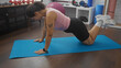 © Krakenimages.com - Young brunette hispanic woman exercising on a mat in a gymnasium with various fitness equipment around.