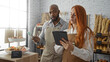 © Krakenimages.com - Man and woman working together in a bakery shop interior while checking inventory on a tablet and holding baking tongs, surrounded by baked goods and bread on shelves