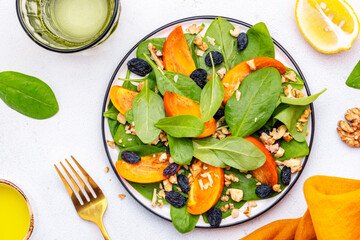 Wall Mural - Wintervegan persimmon salad with walnuts, blue raisin and spinach, white background, top view