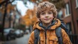 © aritha - A smiling boy in an orange jacket stands outdoors in autumn.