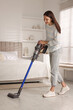 © New Africa - Young woman cleaning floor with cordless vacuum cleaner in bedroom