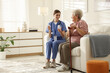 © New Africa - Caregiver giving pills to senior woman on sofa indoors. Home health care service