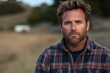 © victoria - A rugged man with a beard poses outdoors in a plaid shirt, exuding confidence and strength.