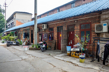 A row of old brick home units with metal roofs in a low-income residential area, with signs of wear and decay. Modest living conditions in a third-world country neighborhood. Poverty in Liuzhou, China