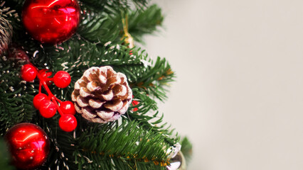 A festive Christmas decoration featuring a frosted pinecone, vibrant red berries, and glossy ornaments nestled within lush green branches.