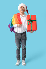 Sticker - Young man in Santa hat with LGBT flag and Christmas gift on blue background