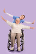 © Pixel-Shot - Happy senior woman in wheelchair with nurse on lilac background