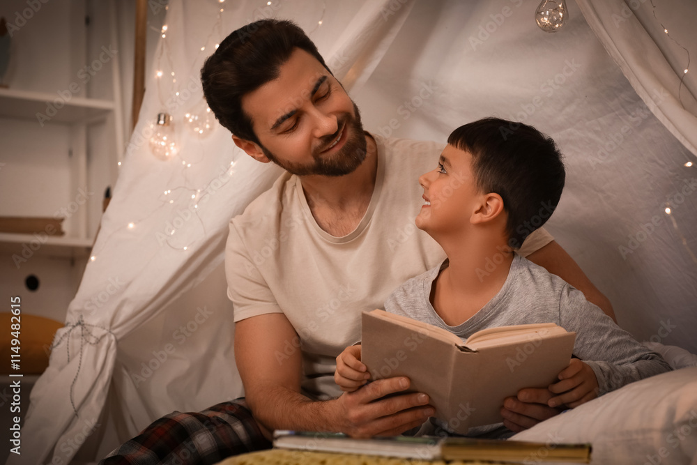 Father with his little son reading book in hut at home
