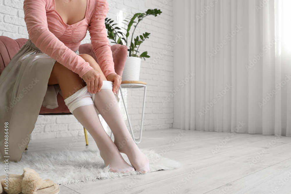Young woman putting on white tights while sitting in armchair