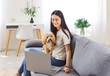 © Studio Romantic - Happy woman spends leisure time online, using a laptop while sitting on the couch with dog at home. She enjoys entertainment and relaxation with domestic animal through internet access.