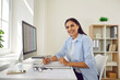 © Studio Romantic - Portrait of a happy smiling business woman accountant sitting at the desk and working on a pc computer with tables and charts at modern office or at home and looking at the camera.