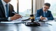 © Vilaysack - A close-up of a gavel on a table with two attorneys discussing legal matters, emphasizing the courtroom setting and the importance of justice.