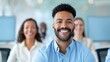 © Vilaysack - A smiling man sits in a modern office, surrounded by colleagues, conveying a sense of teamwork and positivity.
