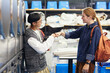 © Seventyfour - Side view of happy Asian man bumping fists with female friend meeting at self service laundry while washing clothes and waiting for result