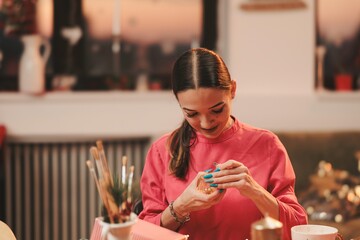 In a warm, inviting indoor setting, a woman carefully decorates a handmade ornament, immersed in the spirit of Christmas. The ambiance reflects joy and creativity