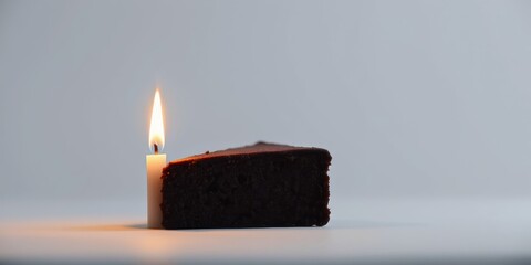 Wall Mural - A single lit candle beside a slice of decadent chocolate cake on a plain white background