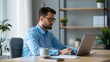 © Vilaysack - A focused man works on a laptop at a modern desk, surrounded by plants and shelves, embodying a productive home office environment.