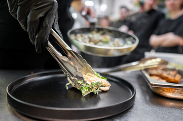 Wall Mural - A chef uses tongs to plate a dish in a busy kitchen, showcasing culinary skills. The scene features fresh ingredients and a professional atmosphere, perfect for food-related content.