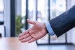 © Ari - A hand is reaching forward to shake hands or support, office environment
