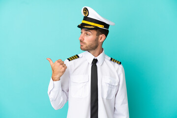 Poster - Airplane caucasian pilot isolated on blue background pointing to the side to present a product