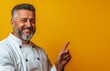 © ArtCookStudio - Chef smiles and points in front of bright yellow backdrop in a professional kitchen setting