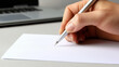 © W - A hand holding a pen writing on a blank paper on a desk