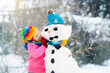 © famveldman - Kids build a snowman in winter park. Snow fun.