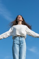 A woman is standing in the open air with her arms outstretched, looking up at the sky. Concept of freedom and joy, as the woman is enjoying the beautiful day and the clear blue sky