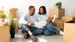 © Prostock-studio - Loving young family thinking about home design, holding apartment plan and working on design for their own house, sitting on floor among boxes with belongings, copy space