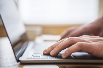 Wall Mural - Set against a blurry office backdrop, the image captures a man's hands in close detail, typing on a cutting-edge laptop keyboard