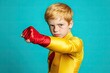 © Kien - A young boy dressed as a superhero, wearing a red and yellow costume with a lightning bolt emblem on the chest, isolated against a turquoise background