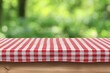 © Muhammad - Red checkered tablecloth on wooden table with blurred green background.