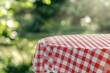 © Muhammad - Red and white checkered tablecloth on a round table outdoors, blurred green background.