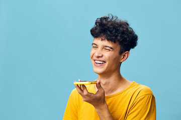 Wall Mural - Smiling young man with curly hair speaking into a smartphone on a light blue background, exuding joy and positivity, showcasing modern communication and technology