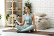 © Pixel-Shot - Sporty young woman with tape measure and bottle of water sitting on mat at home