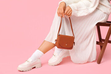 Wall Mural - Young African-American woman with stylish brown handbag sitting on chair against pink background