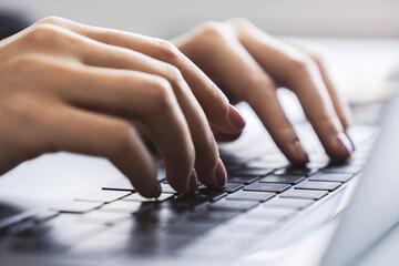 Wall Mural - Woman's fingers nimbly typing on a cutting-edge laptop keyboard, with a blurred office scene behind