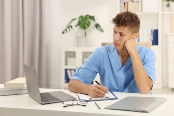 Wall Mural - Medical student taking notes while studying at table indoors