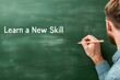 © Pixelbiz - New Year's resolutions personal goals skills concept. A person writes 'Learn a New Skill' on a chalkboard, emphasizing the importance of skill development and lifelong learning.