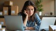 © saranya - woman appears frustrated disappointed at desk surrounded by a laptop and cardboard boxes, likely overwhelmed with work or e-commerce tasks. The cluttered desk reflects her stress and focus.