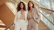 © Sinechana - 87.Two brunette women in stylish office-casual attire, posing on an elegant staircase in a modern interior; each wears a classic blouse and pants suit, accessorized subtly for a sophisticated yet