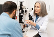 © Maria Vitkovska - Senior female doctor performing eye exam on male patient using slit lamp