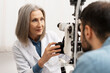 © Maria Vitkovska - Senior female ophthalmologist performing eye exam on male patient using slit lamp