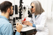 © Maria Vitkovska - Senior female doctor performing eye exam on male patient using slit lamp