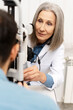 © Maria Vitkovska - Senior female doctor performing eye exam on patient using phoropter in ophthalmology clinic