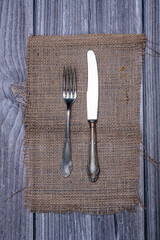 Top view of alpaca metal knife and fork on burlap tablecloth.