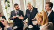 © master1305 - Elderly businessman engaged in lively conversation with young team colleagues during coffee break in modern office. Exchange of experience. Concept of business, communication, teamwork, cooperation